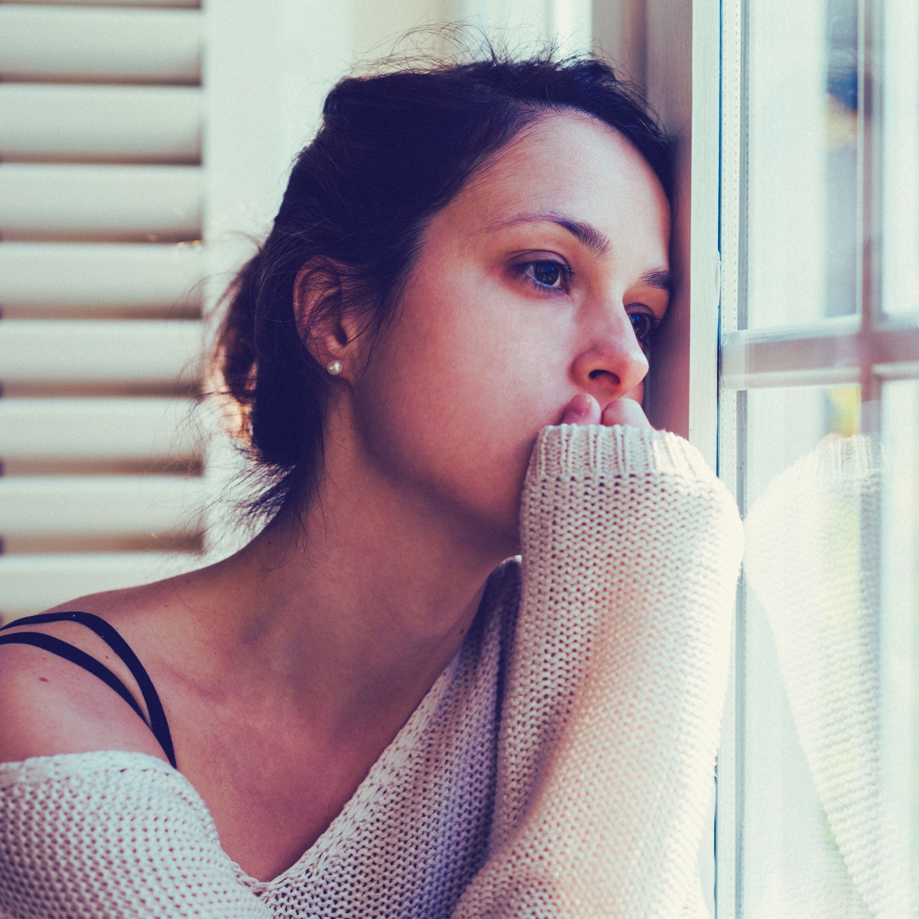 woman looking forlornly out window with hand to face, depression